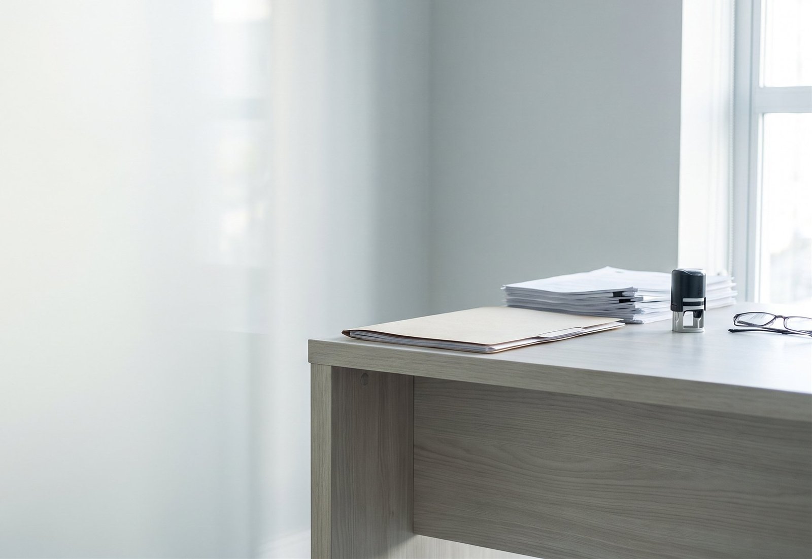 Mesa de trabalho com documentos veiculares, carimbo e óculos, sob luz natural