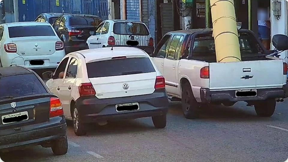 Registro de câmera em via urbana com veículos em circulação, placas cobertas